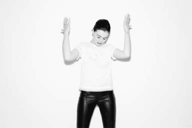 Anne Hathaway in a white t-shirt and black pants posing with hands raised against a white background by Peter Yang