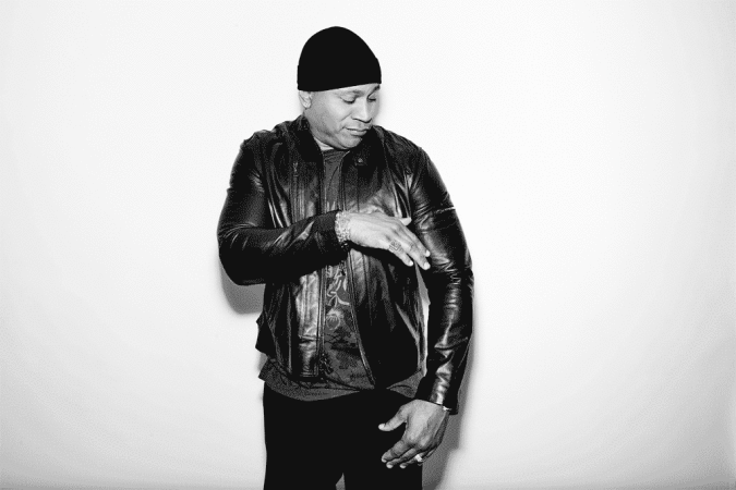 LL Cool J wearing a black leather jacket and beanie, posing against a white background in a black and white portrait.