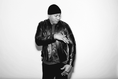 LL Cool J wearing a black leather jacket and beanie, posing against a white background in a black and white portrait.