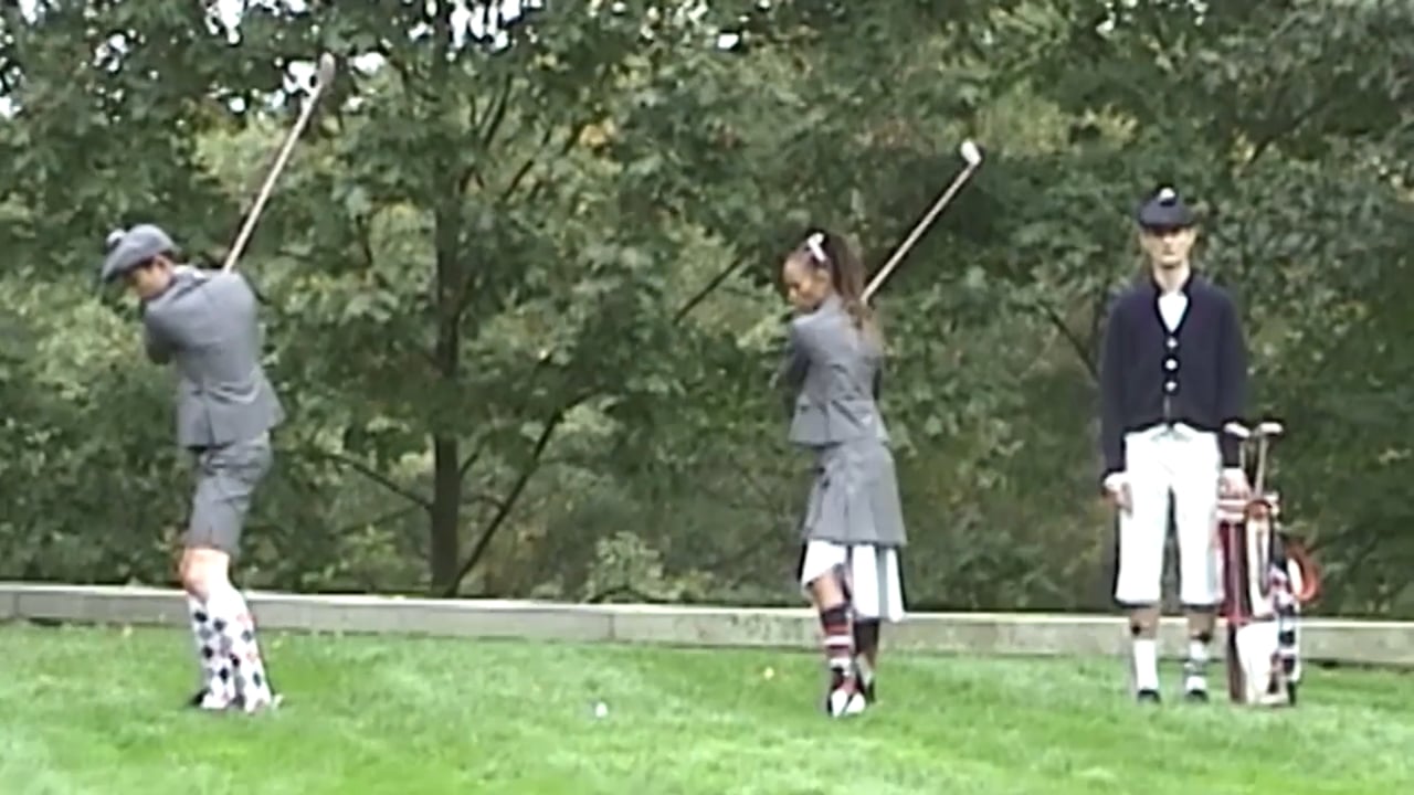 Three golf players in vintage outfits stand on a green, grassy course on a bright day with a backdrop of lush trees and golf equipment.
