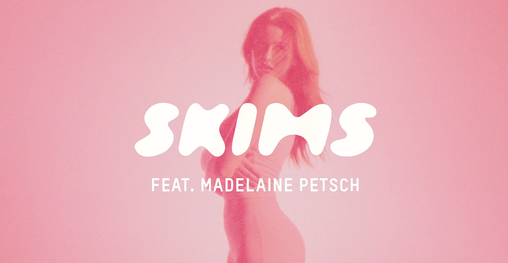 Woman in a pinkish monochromatic studio setting with arms crossed, featuring SKIMS brand logo and Madelaine Petsch.