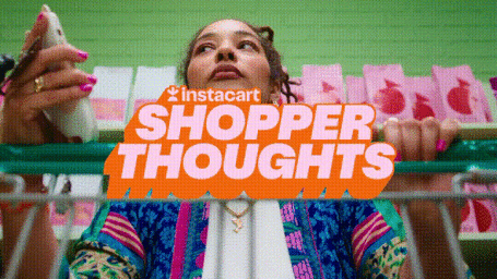 Low angle shot of a woman pushing a shopping cart in a supermarket with pink products on shelves behind her