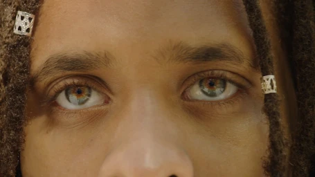 Extreme close up portrait of a person's eyes with dreadlocks and silver hair cuffs.