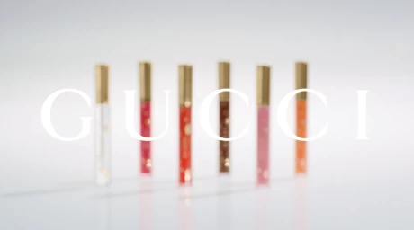 Six slim cosmetic tubes with gold caps arranged upright on a reflective white surface under soft lighting.
