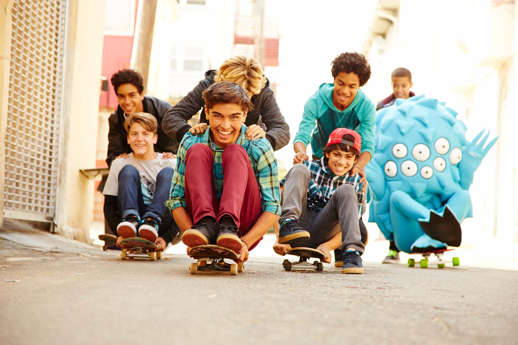 Group of young people on skateboards enjoy an urban outdoor setting, smiling and pushing each other on the street on a sunny day.