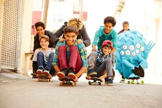 Group of young people on skateboards enjoy an urban outdoor setting, smiling and pushing each other on the street on a sunny day.