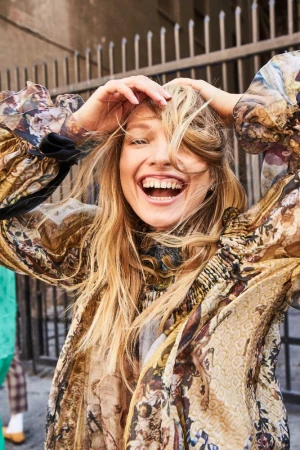Smiling blonde woman with her hands in her hair wearing a patterned floral top outdoors in Los Angeles.