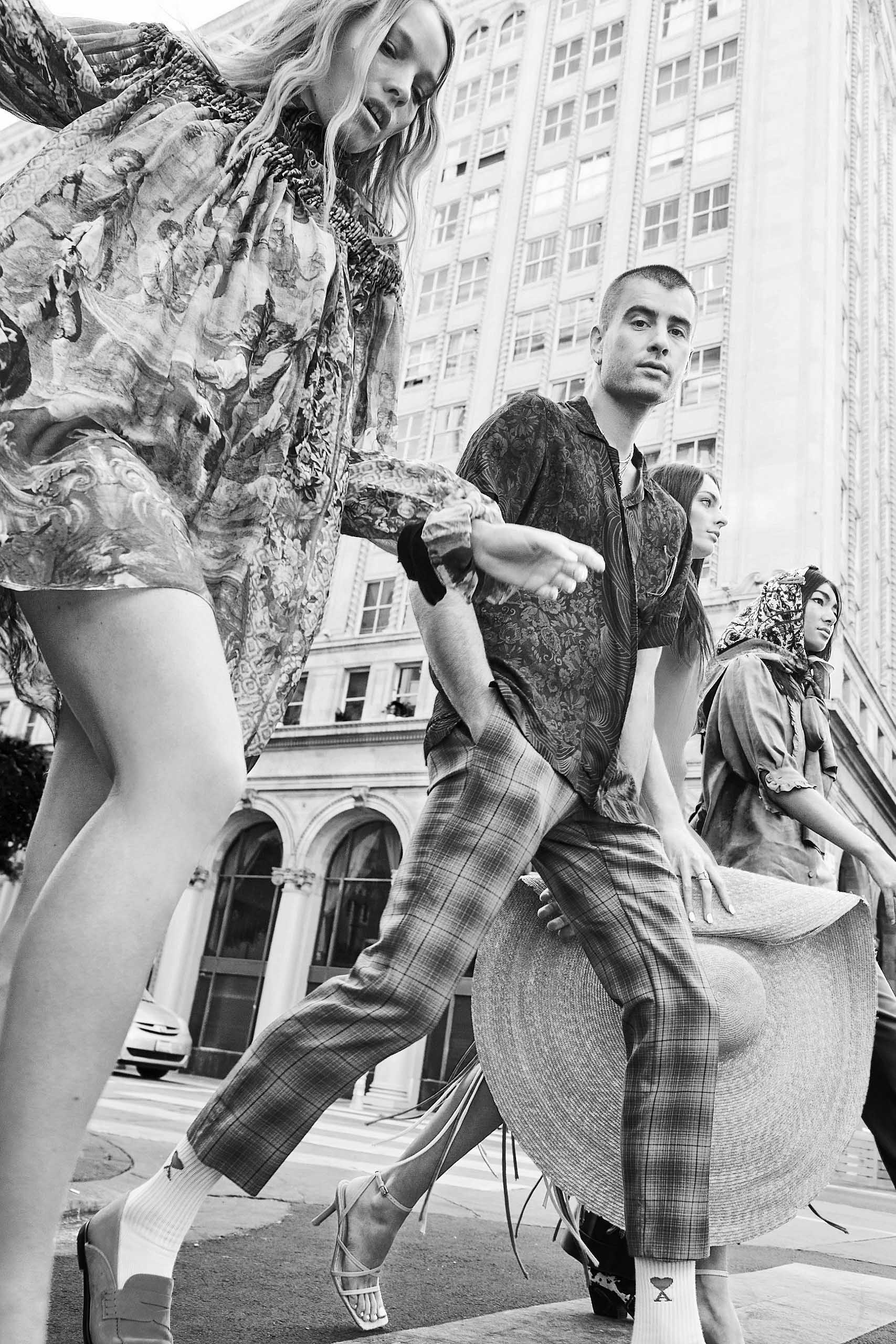 Black and white fashion shot of four people walking on a city street near tall buildings, showcasing vintage patterns and textures.