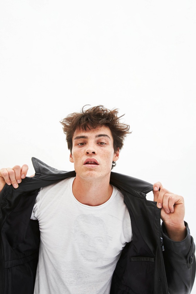 Young man with messy dark hair wearing a white t-shirt and a black leather jacket against a white background