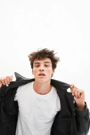 Young man with messy dark hair wearing a white t-shirt and a black leather jacket against a white background