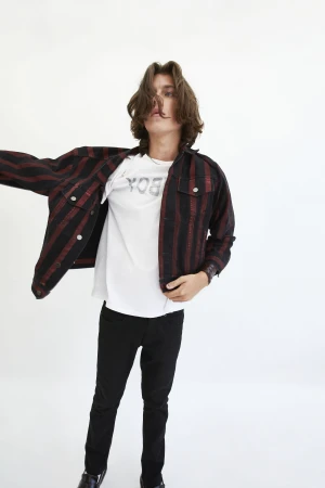 A young male model with long dark hair wearing a striped jacket, white t-shirt, and black jeans against a seamless white background.