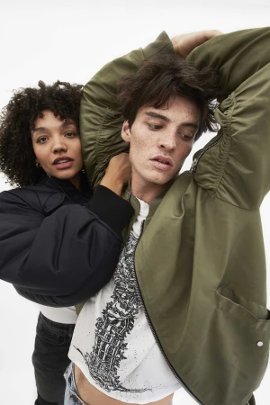 Two models posing together, a woman in dark jacket and a man in an olive green bomber jacket
