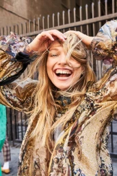 Smiling blonde woman with her hands in her hair wearing a patterned floral top outdoors in Los Angeles.