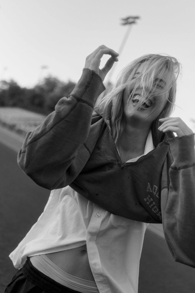 Monochrome close-up portrait of a woman laughing while wearing a cropped sweatshirt and white shirt, with an outdoor background.