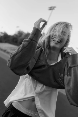 Monochrome close-up portrait of a woman laughing while wearing a cropped sweatshirt and white shirt, with an outdoor background.