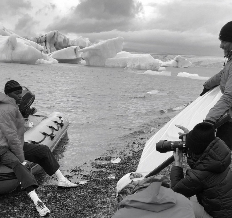 Black and white image of a film crew photographing icebergs by the water. A boat and camera equipment are visible in the frame.