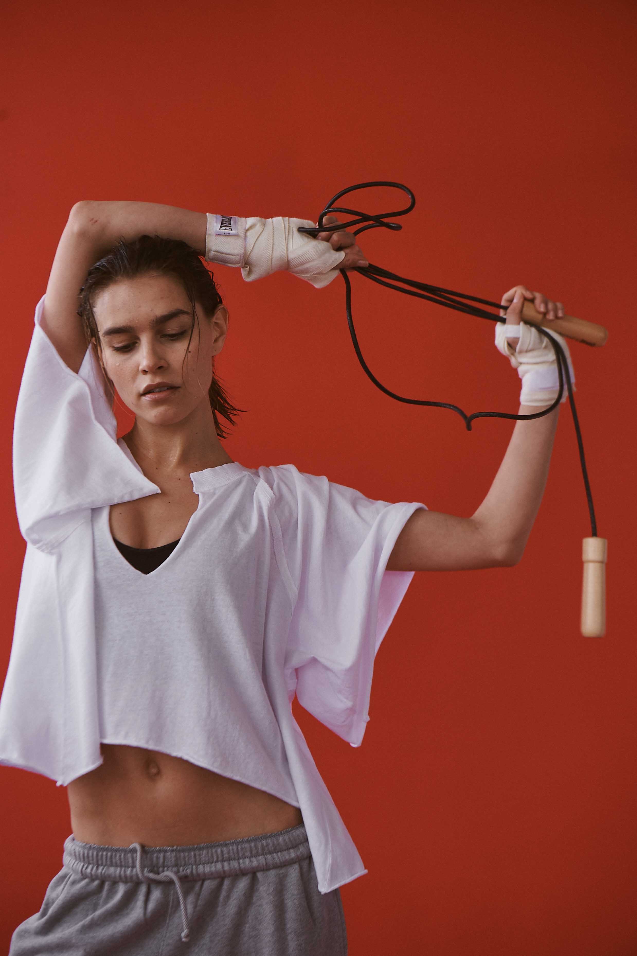 Athletic woman in sportswear poses with a jump rope against a red background, showcasing fitness and active lifestyle.