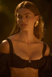 Portrait of a woman with long hair wearing an off-shoulder dark top and gold geometric earrings in golden hour light.