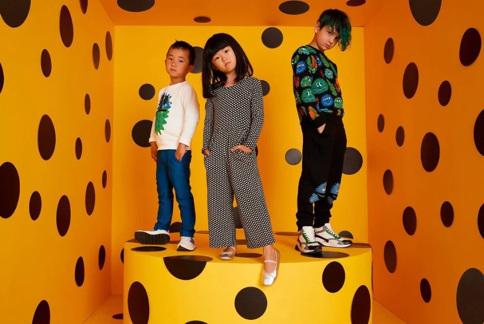 Three children pose on a yellow and black polka dot platform in a matching polka dot room, showcasing youthful fashion and style.