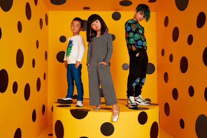 Three children pose on a yellow and black polka dot platform in a matching polka dot room, showcasing youthful fashion and style.