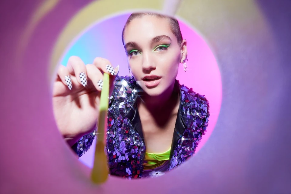 Close-up of a stylish adult female model holding a spoon, with a pink and blue studio background and a unique point-of-view perspective.