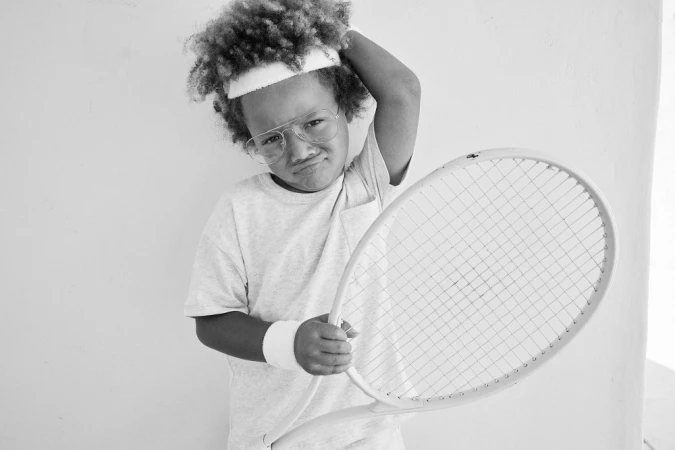 Child wearing glasses and a tennis headband holding a racket, photographed by Don Diaz.