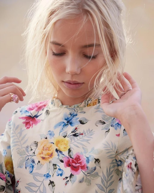 Portrait of a young blonde girl with her eyes closed, wearing a floral top, and soft lighting; shot at eye level with a shallow depth of field.