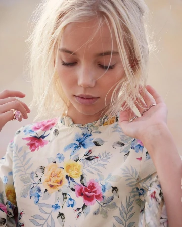 Portrait of a young blonde girl with her eyes closed, wearing a floral top, and soft lighting; shot at eye level with a shallow depth of field.
