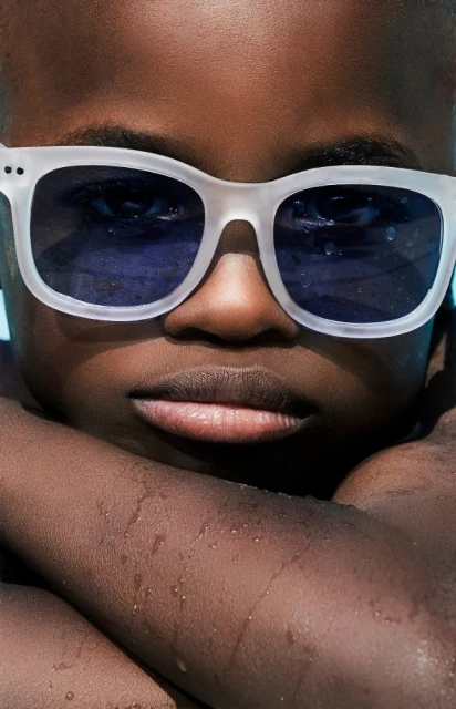 Close-up portrait of a young Black child with white sunglasses, featuring vibrant lighting and a shallow depth of field.