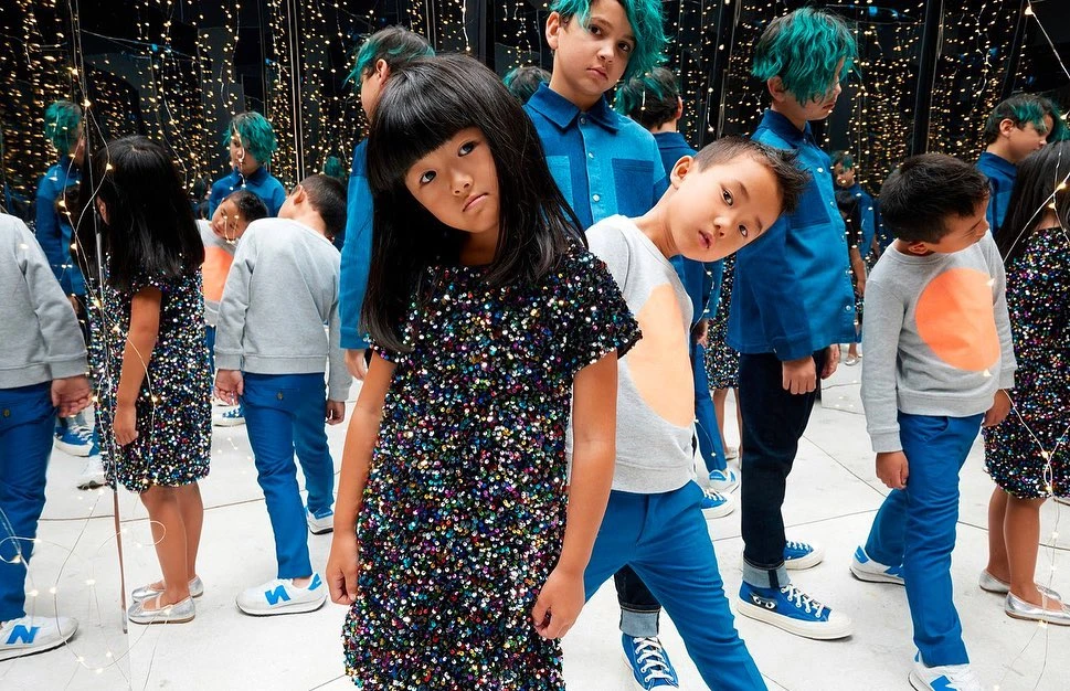 Group of Asian children in a mirrored room with fairy lights, wearing blue and black clothing, posing for a fashion shot.