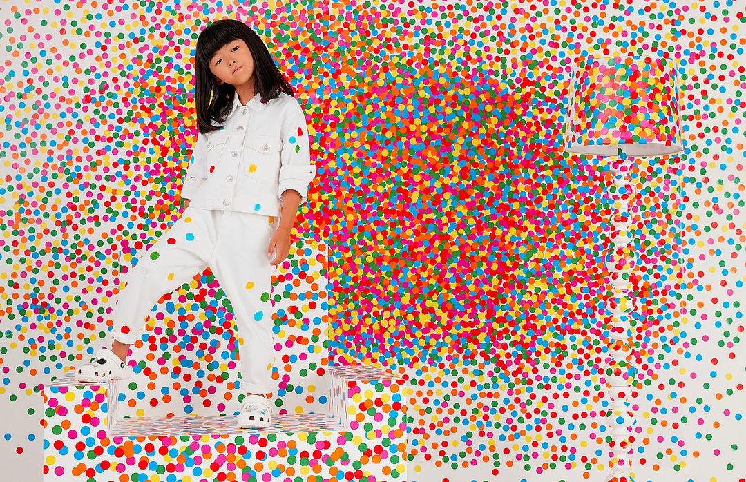 A young Asian girl in white clothing stands on a clear platform against a vibrant confetti background, creating a lively and colorful portrait.