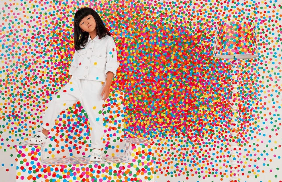 A young Asian girl in white clothing stands on a clear platform against a vibrant confetti background, creating a lively and colorful portrait.