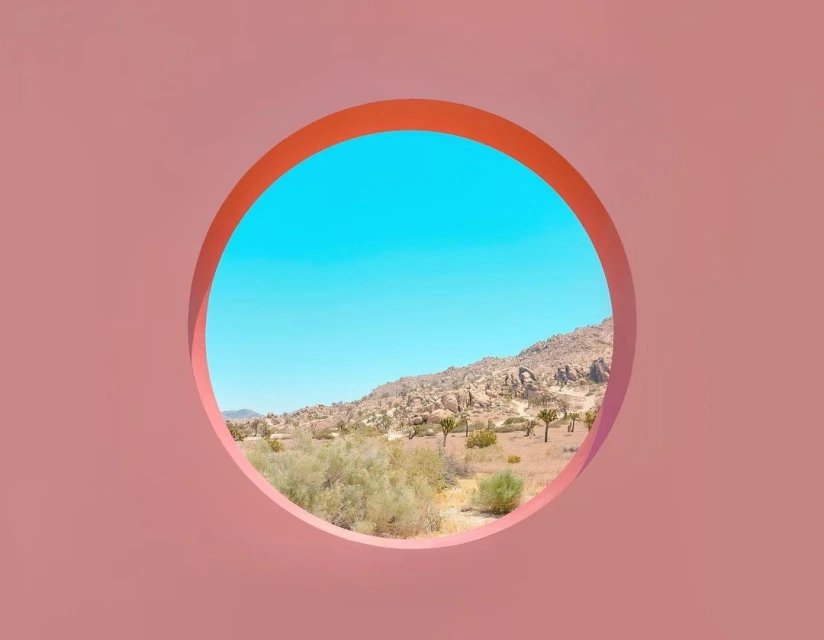 Desert landscape with rock formations viewed through a coral pink circular frame, showcasing natural beauty and unique perspective.