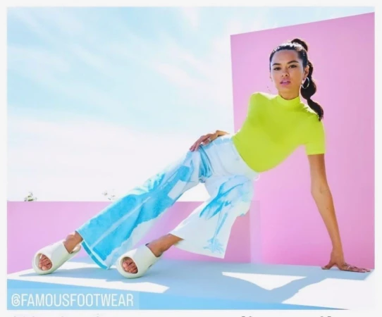 Woman poses in a neon yellow top and white pants with blue palm tree print, paired with platform slide sandals against a bright backdrop.