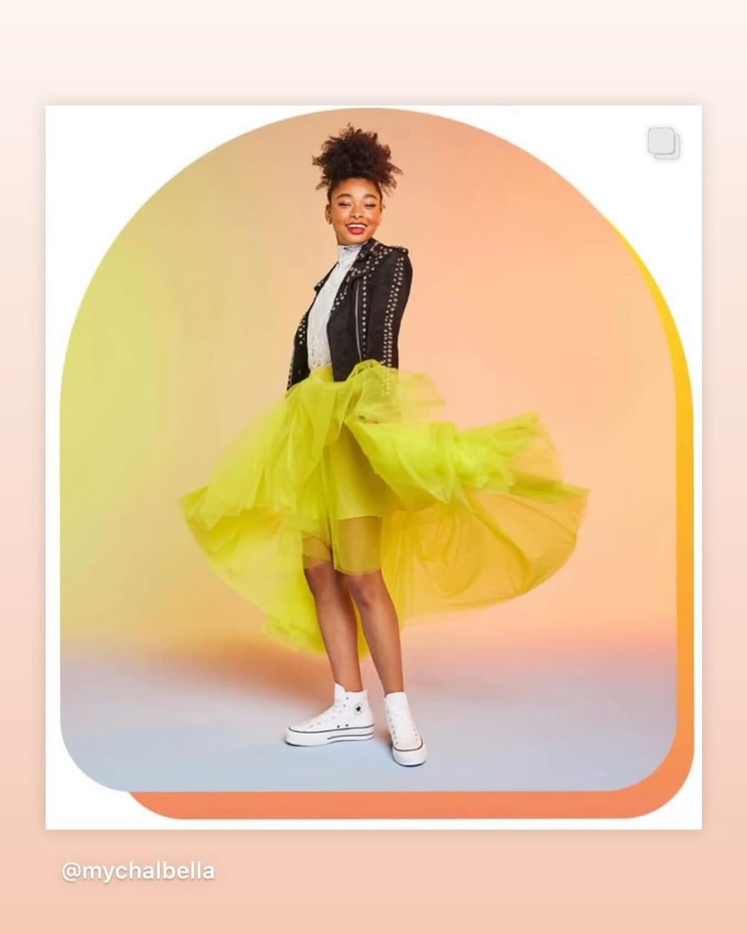 A young adult female poses in studio wearing a black studded jacket, neon yellow tulle skirt, and white platform Converse sneakers.