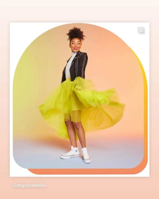 A young adult female poses in studio wearing a black studded jacket, neon yellow tulle skirt, and white platform Converse sneakers.