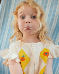 Close-up portrait of a child with blonde curly hair making a funny face against a blue and white striped backdrop