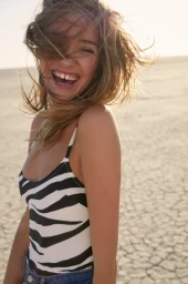 Woman in zebra print top laughing with hair blowing in the wind under bright sunlight against a cracked ground backdrop