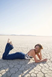 Woman lying on dry cracked desert ground wearing blue jeans and a patterned top, photographed by Don Diaz.