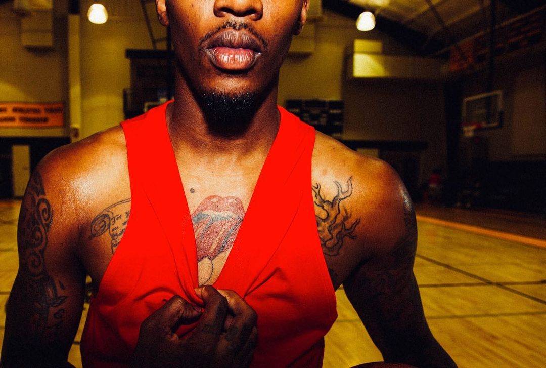 Close up of an athletic African-American man in a red tank top with tattoos on a basketball court. Focus on his face and upper torso.