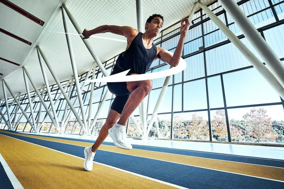 Athlete in motion: A man in sportswear runs on a blue and yellow track inside a bright, modern stadium with large windows.