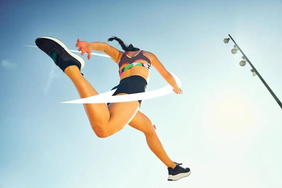 Athletic woman leaps across the finish line with one leg extended high in sportswear against a bright blue sky, athletic shoes.