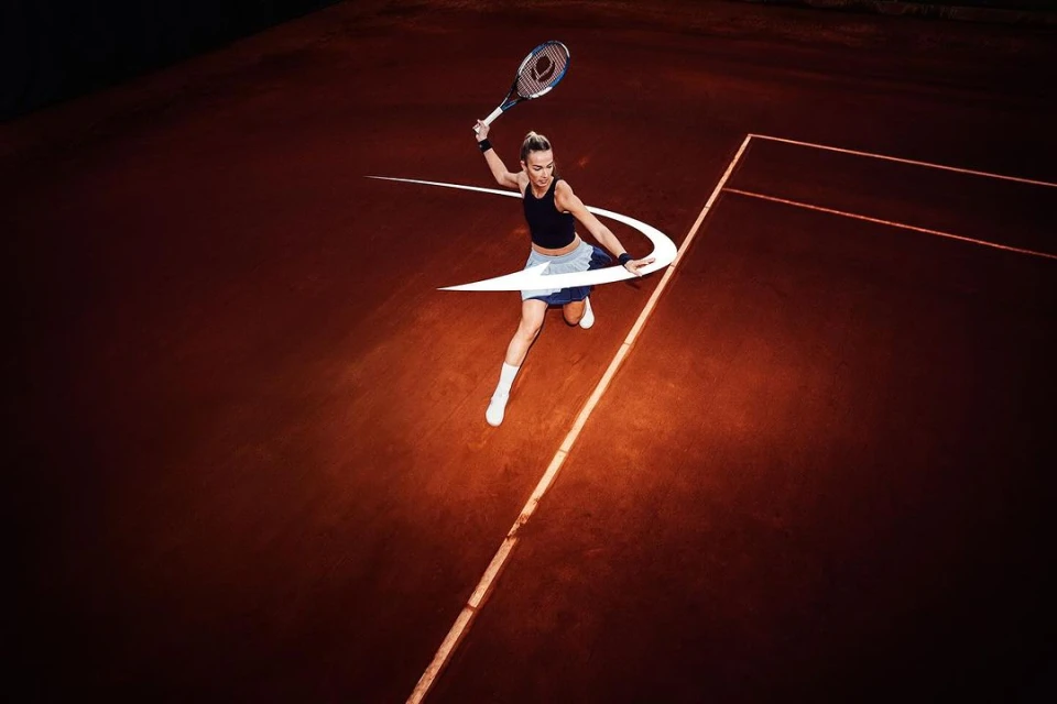 Female tennis player in action on a clay court, hitting the ball with a racket, wearing athletic clothing, with graphic overlay.