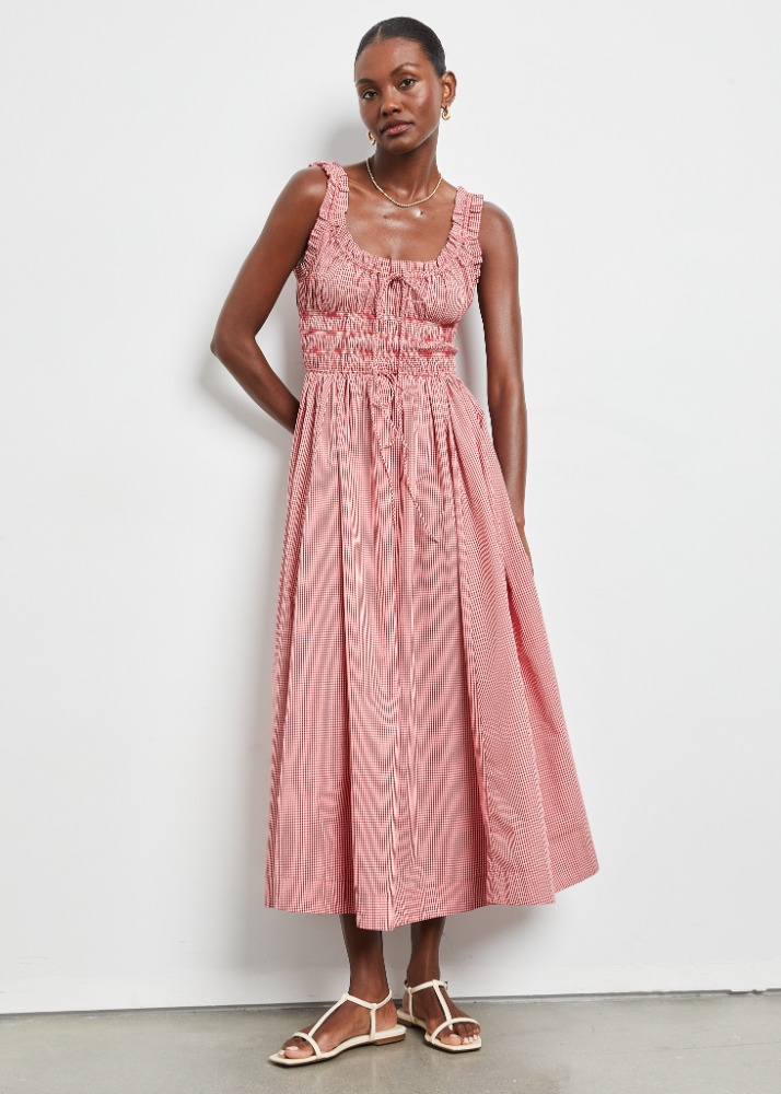 Adult female fashion model poses in a red and white gingham midi dress with spaghetti strap sandals against a neutral backdrop.