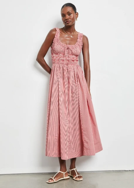 Adult female fashion model poses in a red and white gingham midi dress with spaghetti strap sandals against a neutral backdrop.