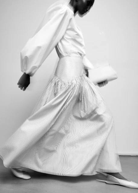 Fashion shot of an African-American woman wearing a white blouse and striped skirt, holding a clutch, with a blurred motion effect.