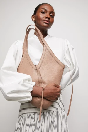 Studio shot of a woman posing with a light brown leather hobo bag, styled with a white blouse and striped skirt against a neutral backdrop.