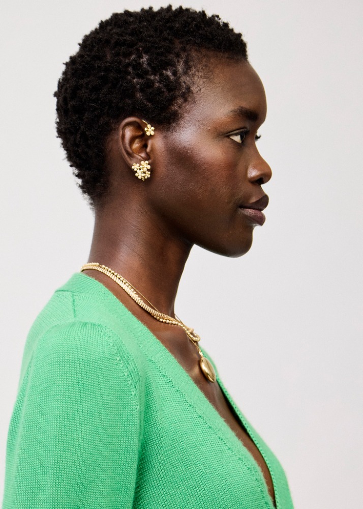 Profile shot of a Black woman with short natural hair wearing a green cardigan and gold jewelry against a neutral background.
