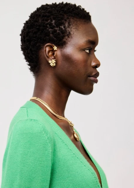 Profile shot of a Black woman with short natural hair wearing a green cardigan and gold jewelry against a neutral background.