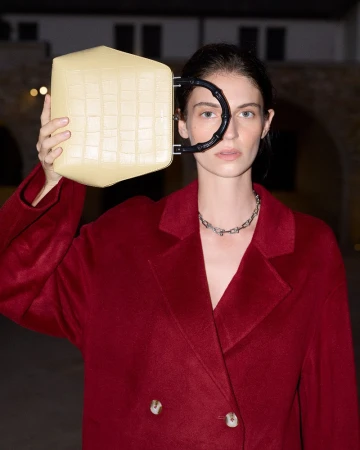 Adult female in a red coat holding a yellow geometric purse with a black handle and wearing a silver necklace outdoors.